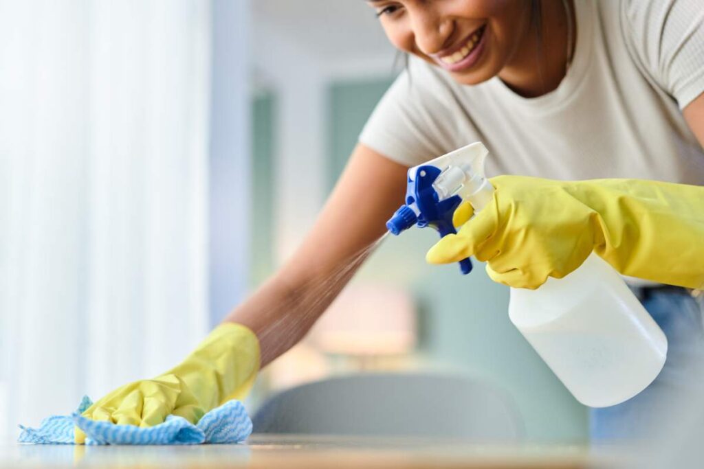 Shot of a young woman wiping a surface while spraying it with product at home.